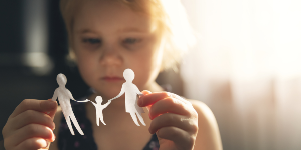 sad child holding paper silhouette of a family in her hands